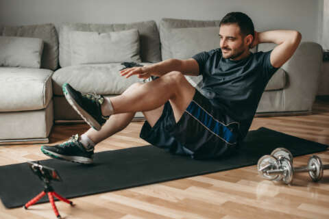 Junger Mann schaut sich Sportügungen auf einem Smartphone an und führt diesw auf einer Matte aus.