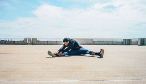 Outdoor-Sport: Mann stretcht sich im Sitzen auf einem Flachdach.