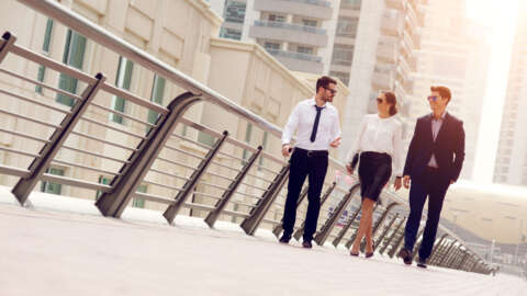 Dresscode: Eine Frau und zwei Männer im Business-Outfit laufen über eine Straße.