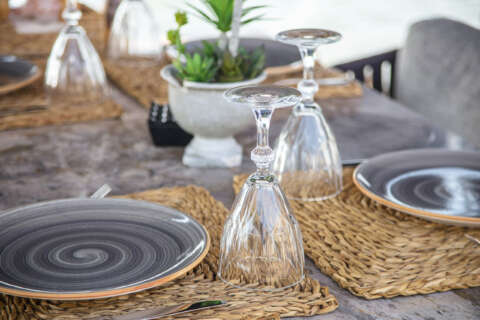 Bedürfnis: Auf einem grauen Holztisch liegen Platzsetz aus Bast. Darauf stehen graue Teller mit Besteck und Gläsern