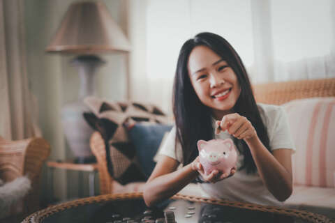 Spar dich glücklich: Mädchen lächelt und wirft 2€ Münze in rosa Sparschwein.