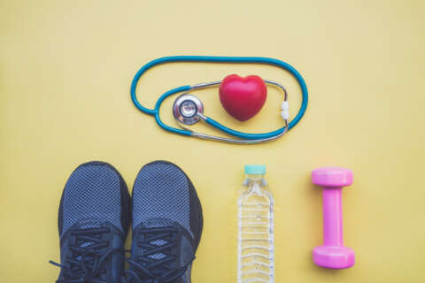 Sport nach Corona: Stethoskop mit Herz, Sportschuhe rosa Hantel und Wasserflasche auf gelbem Grund.